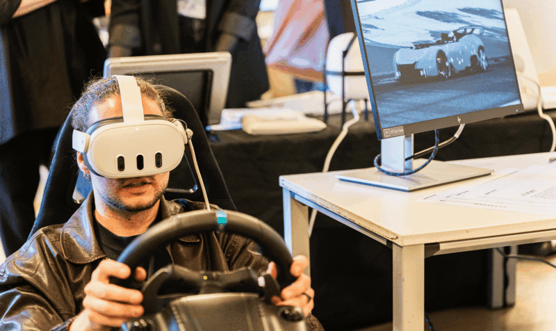 A young man with VR glasses and a steering wheel in his hands