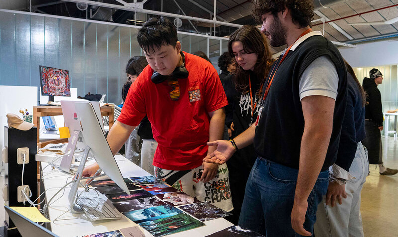 Three people looking at graphic design projects on a monitor inside an exhibition space