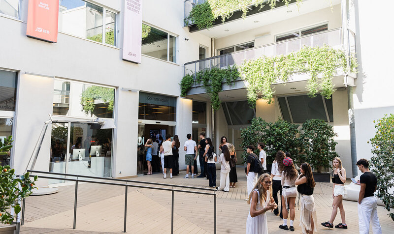 Students queuing in a building's inner courtyard to enter the lobby.