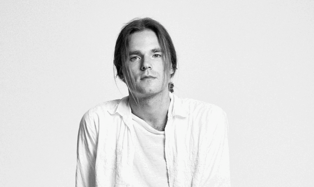 Close-up of a man in a shirt and with light hair looking at the camera. Black and white photo.